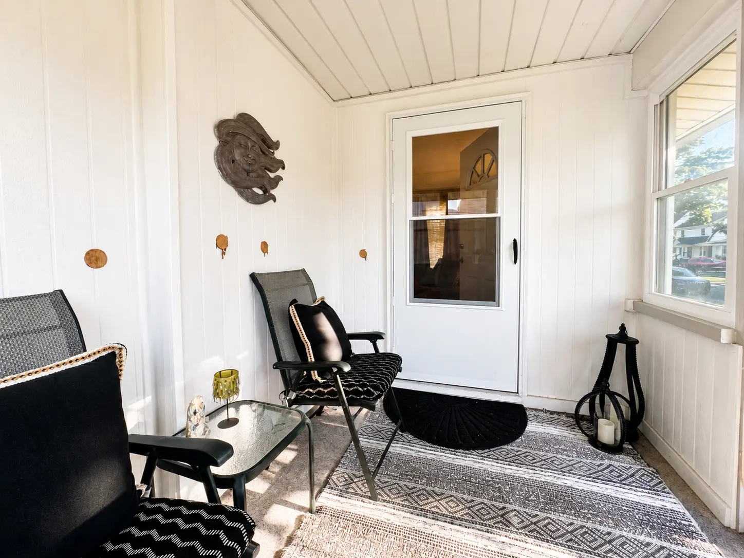Enclosed front porch at 3718 Revere Drive with seating, windows overlooking the street, and the front door