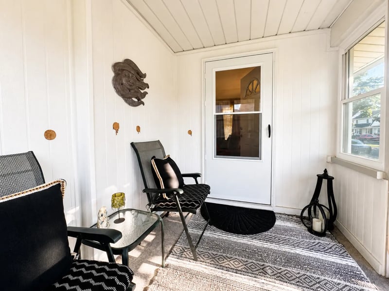 Enclosed front porch at 3718 Revere Drive with seating, windows overlooking the street, and the front door